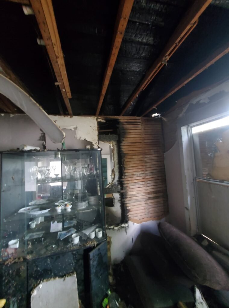Fire-damaged living area with charred ceiling joists and structural damage